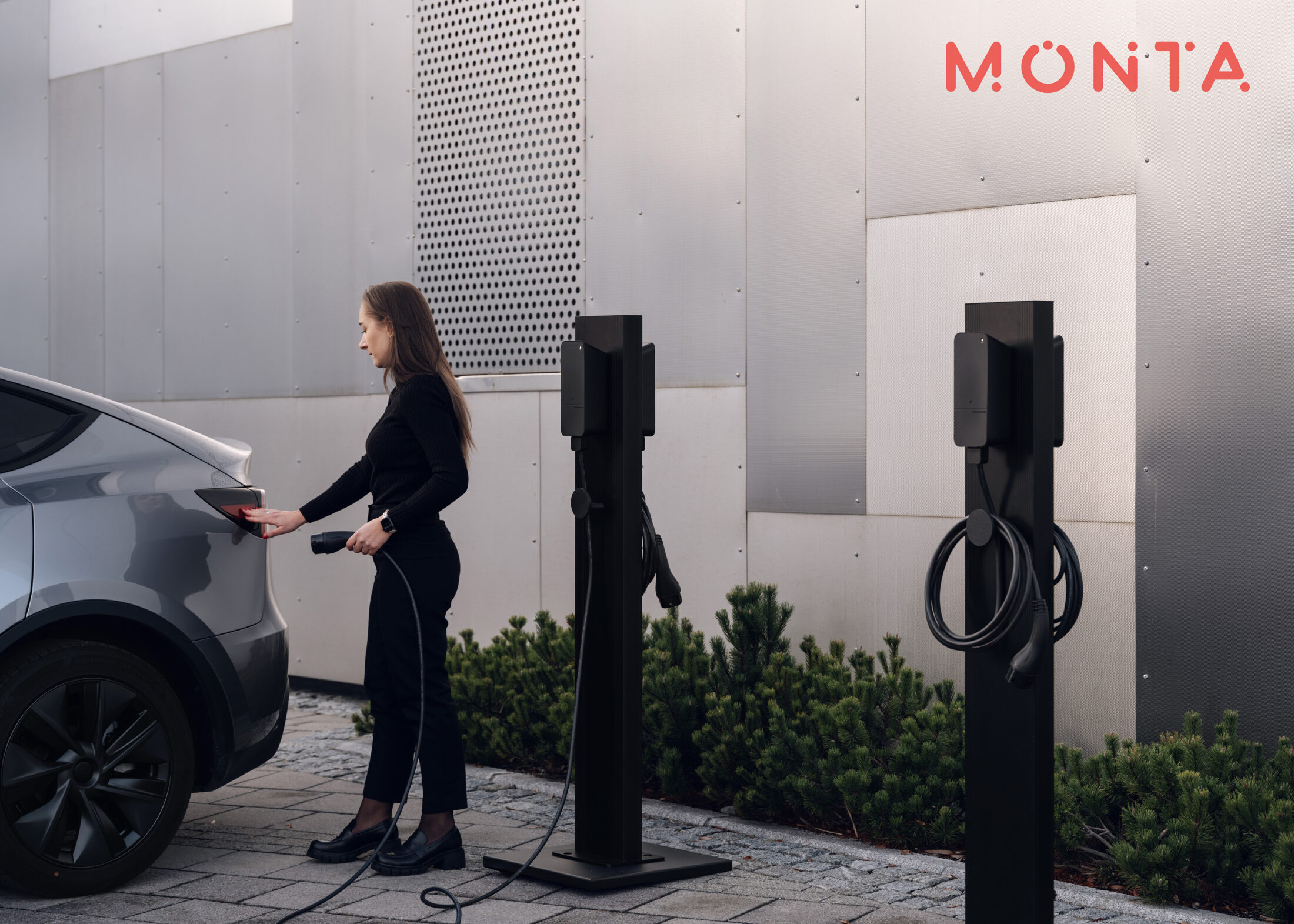 Resident charging an electric car at freestanding amina EV charging stations integrated with Monta CPMS, illustrating open and interoperable charging infrastructure.