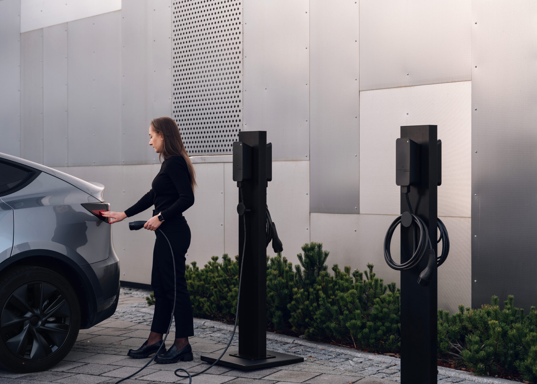 Woman charging electric car at outdoor public charging station with amina C