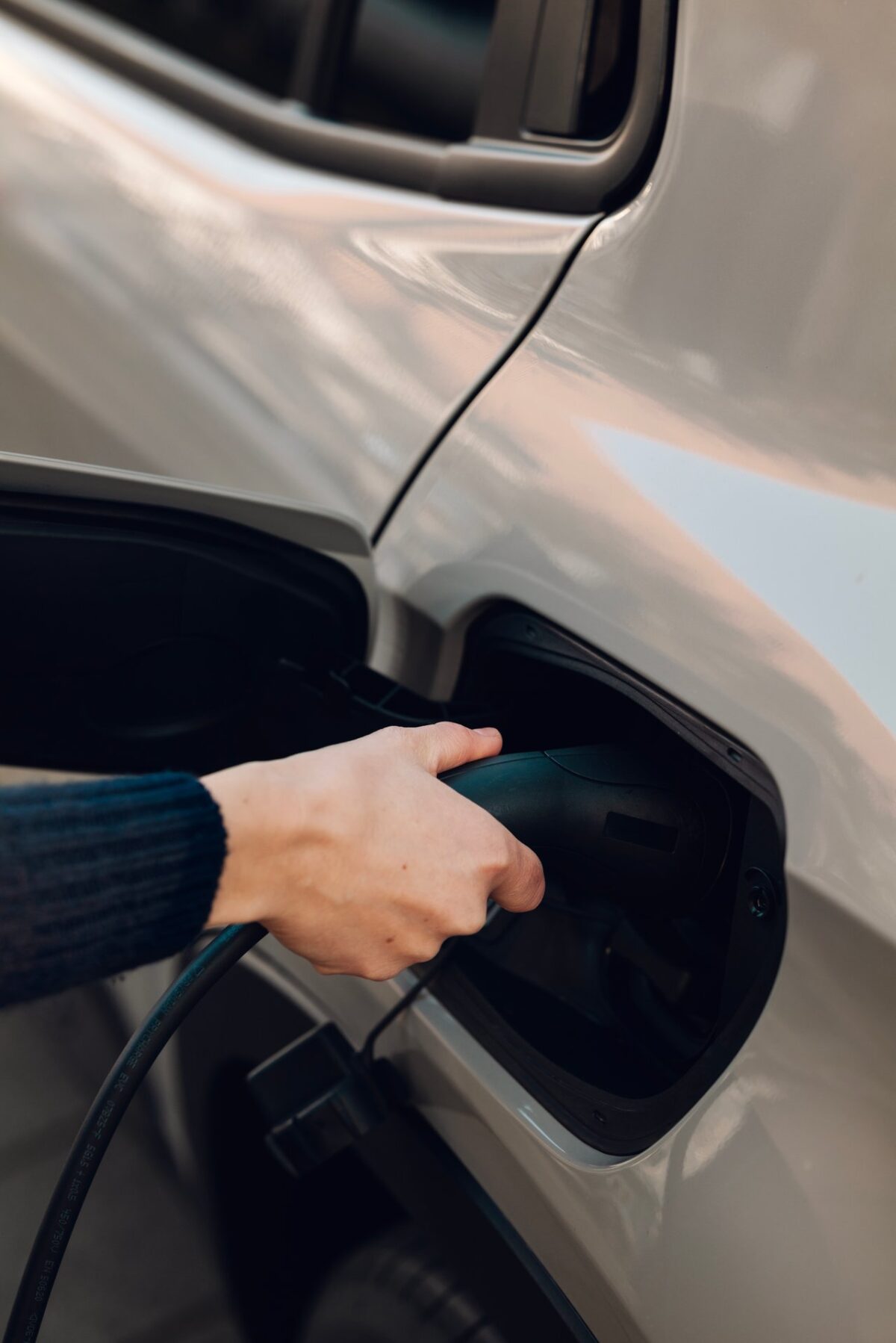 Hand holding blue charging cable near EV charging port