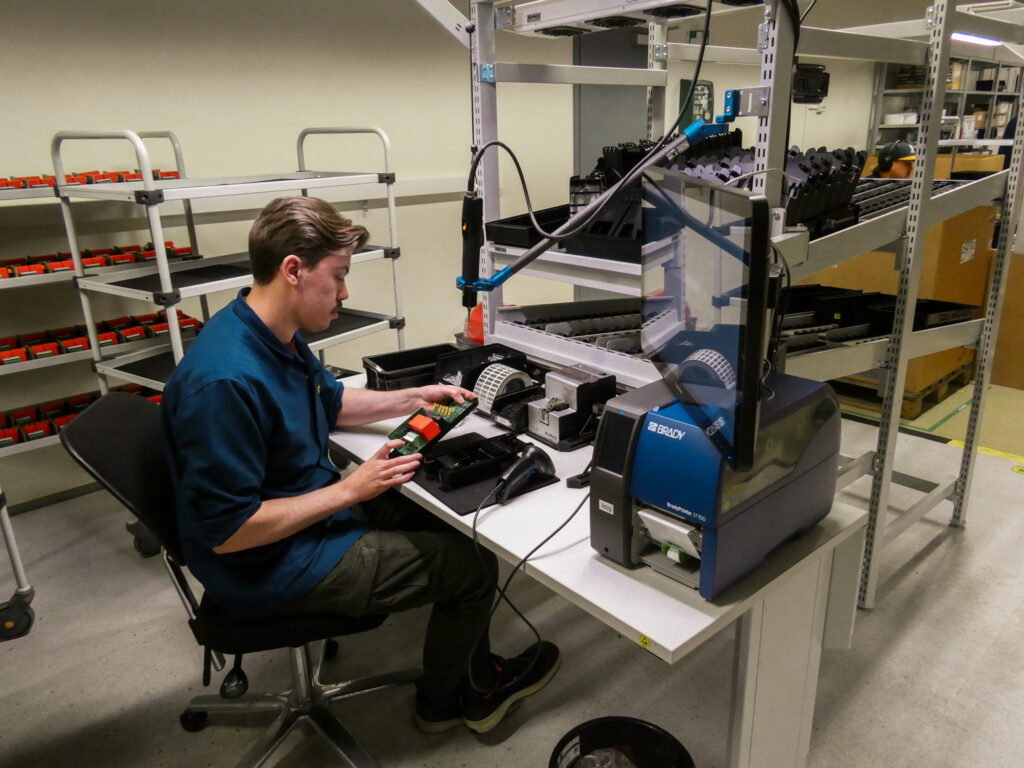 Factory technician inspecting and configuring amina charger electronics at a dedicated workstation, demonstrating hands-on quality assurance before deployment.
