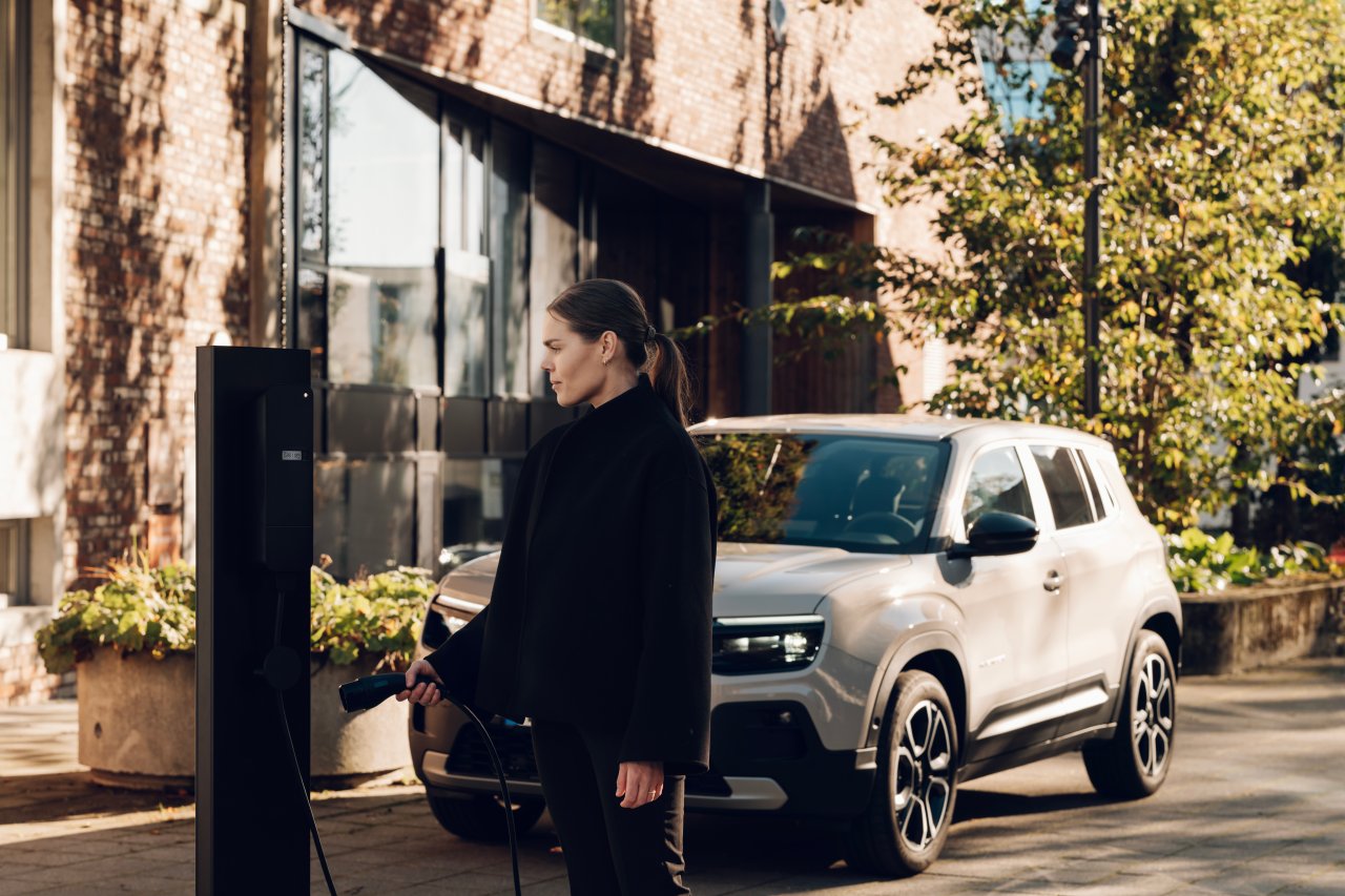 Resident plugging an electric car into an amina EV charging station outside a brick residential building, showing shared charging infrastructure in an urban multi-dwelling environment.