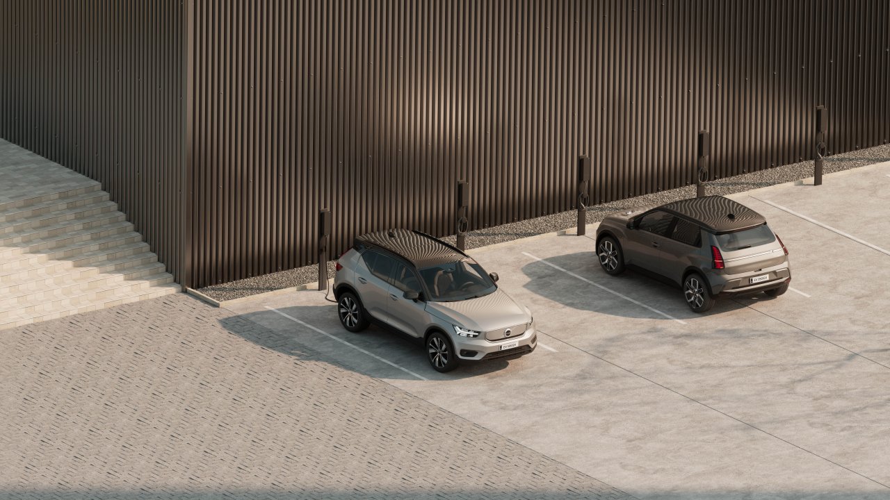 Two electric cars parked in marked bays beside multiple amina M EV charging stations mounted on posts along a commercial building wall, demonstrating scalable shared charging infrastructure for multi-dwelling or workplace environments.