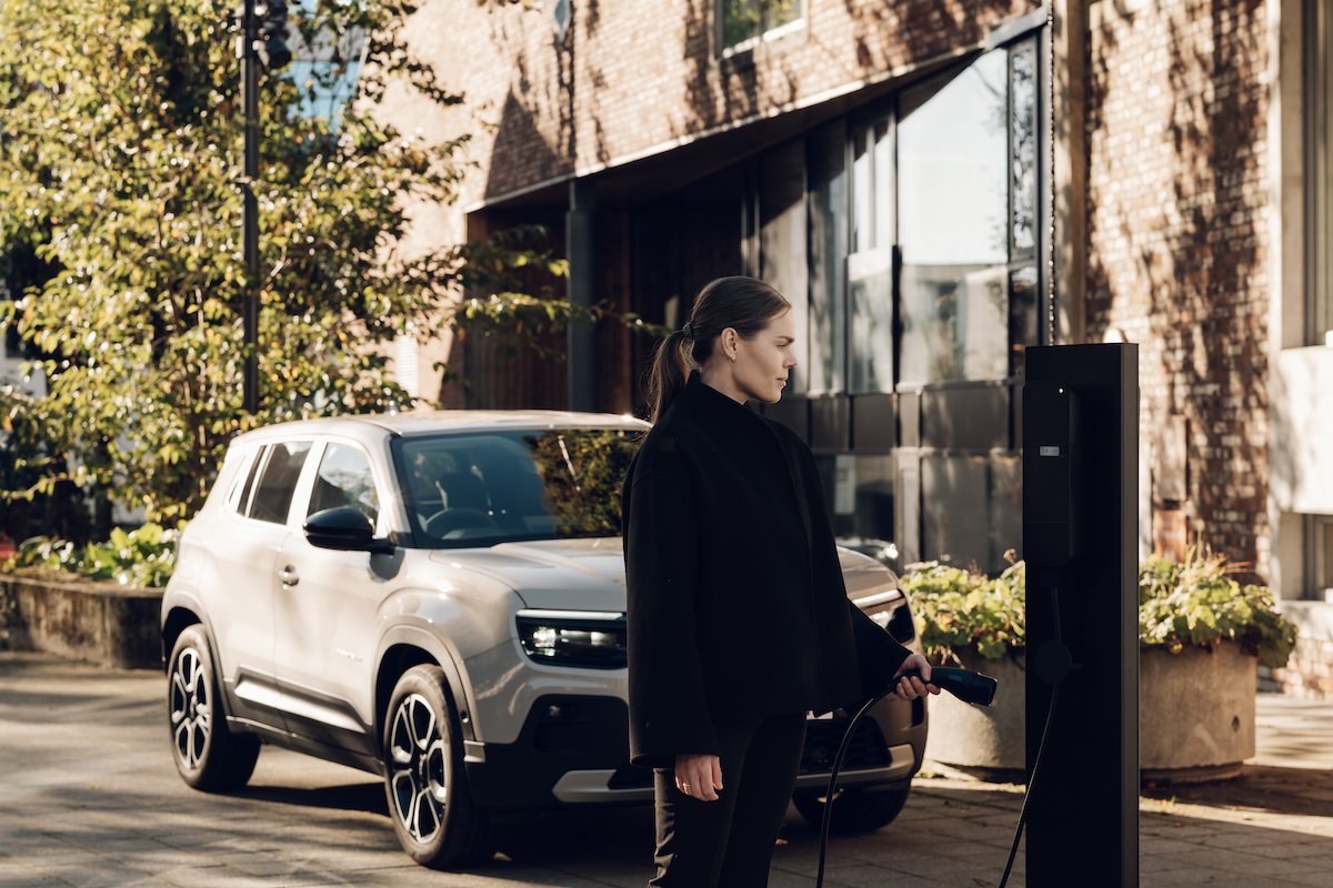 Resident plugging an electric car into an amina M MID certified EV charging station outside a brick residential building, showing shared charging infrastructure in an urban multi-dwelling environment.